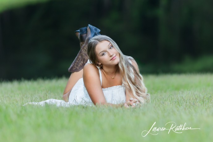 young lady laying in the grass, white dress and cowboy boots 